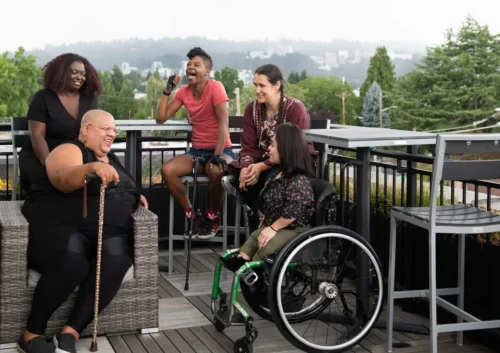 Disabled community members gathered together outdoors on a rooftop patio in the city.